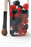 Make-up brush next to cosmetic jar filled with red and black currants