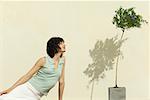 Woman sitting outdoors, leaning toward flowering plant, eyes closed