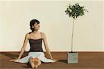 Woman sitting on the ground beside potted plant, smiling, eyes closed