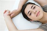 Female lying on pillow, arms raised, smiling at camera