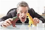 Homme d'affaires jouant avec des jouets dinosaures sur le Bureau