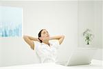 Woman leaning back at desk, hands behind head, eyes closed