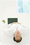 Businessman lying on back in office, head dangling, eyes closed