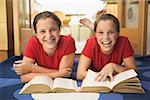 Twin teen girls smile while doing their homework.