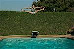 Teenage girl does the splits while jumping into a swimming pool.