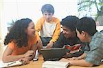 Quatre enfants adolescents travaillant sur un ordinateur portable et l'école des livres.
