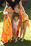 Mother wrapping her three children in a towel outdoors.