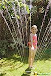 A young girl standing in a sprinkler.