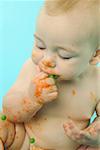 Infant eating baby food with fingers.