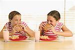 Twin teenage girls eating hamburgers.
