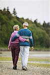 Couple walking on the beach with their arms around each other.