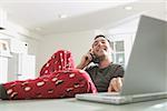 Man in pajamas talking and working on a laptop.