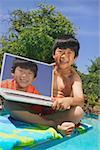A young boy poolside with a laptop computer