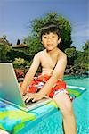 A boy sitting on a diving board with his laptop