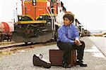 Boy at train station sitting on suitcase