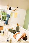 Woman painting walls while man rests