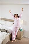 Woman in pajamas stretching next to bed