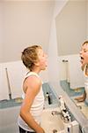 Boy looking at tongue in bathroom mirror