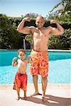 Father and son flexing muscles by pool