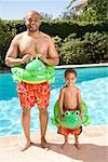 Father and son wearing identical flotation devices by pool