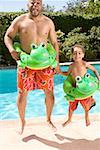 Father and son wearing identical flotation devices by pool