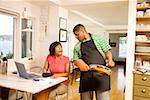 Man cleaning a pan as wife writes checks