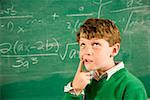 Boy thinking in front of math on blackboard