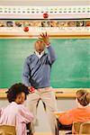 Male teacher juggling apples in classroom
