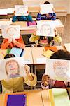Students holding drawings over faces in classroom