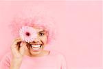 Woman wearing pink wig and holding flower over eye