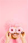 Woman wearing pink wig and holding flowers over eyes