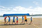 Male camp counselor and children carrying canoe