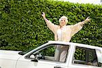 Senior woman standing in sunroof of car
