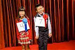 Asian girl and boy wearing prize ribbons on stage