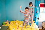 Asian siblings jumping on bed