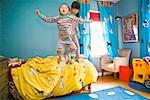 Asian siblings jumping on bed