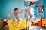 Asian siblings jumping off bed