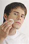 Young male adult cleaning face with cotton pad