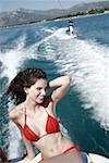 Female young adult on speedboat; male waterskiing