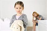 Cheerless girl looking at camera, mother sitting in background