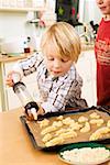 Boy piping biscuit dough onto baking tray with biscuit syringe