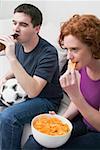 Jeune couple avec le football, bouteille de bière & des chips en regardant la télévision