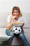 Young woman with football and snack food watching TV