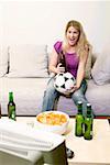 Young woman with football and bottle of beer watching TV