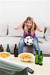 Young woman with football, beer bottles & crisps watching TV