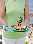 Woman holding plate of crab claws and dip on beach