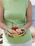 Woman holding plate of crab claws and dip on beach