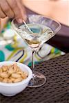 Woman holding green olive on cocktail stick in Martini glass