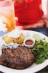 Woman holding plate of steak, baked potato, salad & sauce