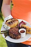 Woman holding a plate of grilled steak and accompaniments